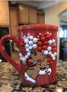 a red coffee mug decorated with beads and pearls on top of a granite countertop