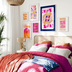 a bedroom with pink and orange bedding, pictures on the wall and paintings above it