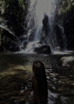 a woman standing in the water next to a waterfall