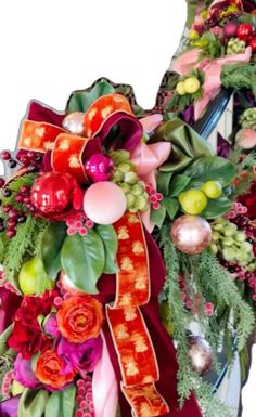 a christmas wreath with red, green and pink flowers on it's side next to a mirror