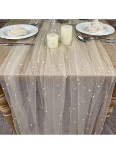 a table topped with plates and candles next to a white plate covered in sheer fabric