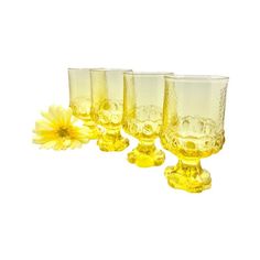 four yellow glass goblets sitting next to each other with a flower in the middle