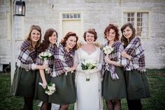 a group of women standing next to each other in front of a brick building holding bouquets