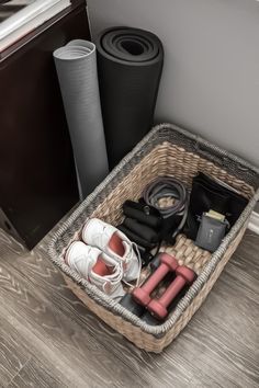 a basket filled with shoes and other items on top of a wooden floor next to a black trash can