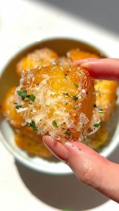 a person holding food in their hand on top of a white plate with oranges and parmesan cheese