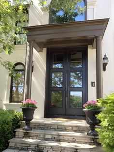 the front entrance to a house with two planters on the steps and one door open