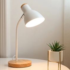 a white table lamp sitting on top of a wooden stand next to a potted plant