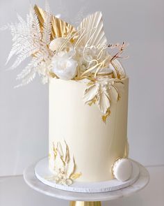 a white and gold wedding cake with flowers on the top is sitting on a stand