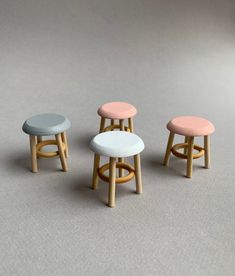 three stools in different colors on a gray surface with white and pink cushions,