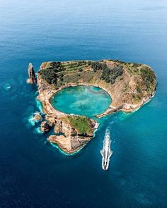 an island in the middle of the ocean with a boat coming towards it and another boat approaching