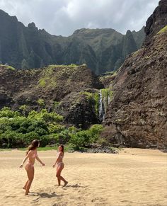 two women in bikinis playing with a frisbee on the beach near a waterfall