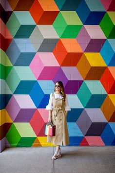 a woman standing in front of a colorful wall holding shopping bags and looking at the camera