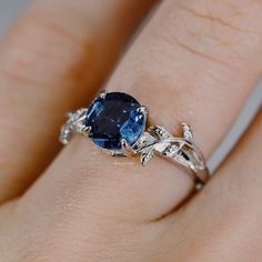 a woman's engagement ring with a blue stone in the center and leaves around it