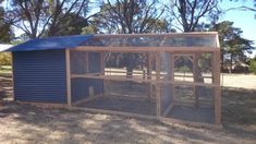 a blue chicken coop in the middle of a field with trees and grass behind it