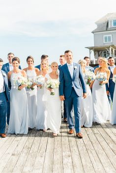 a bride and groom with their bridal party on the dock in front of a house