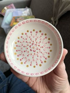 a person holding a white bowl with pink and gold dots on it in their hand