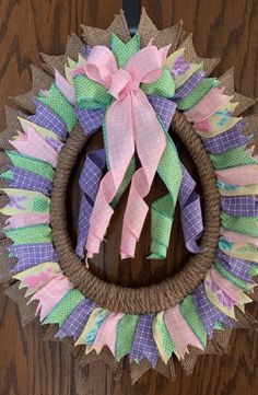 a wreath with pink, green and purple ribbons hanging on a wooden door hanger