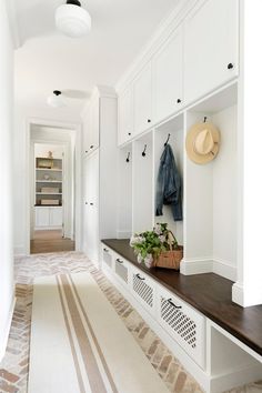 a long hallway with white cabinets and wooden bench in the center, along with an area rug on the floor