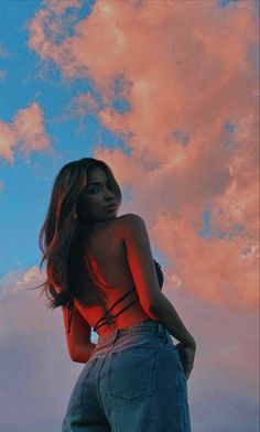 a woman is standing in front of the sky with her back turned to the camera