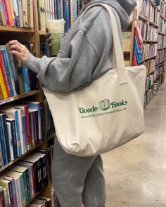 a person with a book bag standing in front of a bookshelf holding a cup