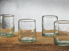 four glasses sitting on top of a wooden table next to each other and one is empty