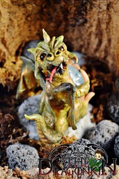 a small figurine sitting on top of rocks in the dirt with it's mouth open