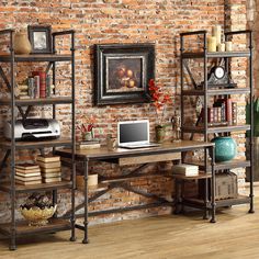 a computer desk sitting in front of a brick wall with bookshelves on it