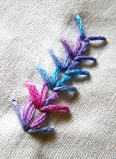 three different colored thread flowers on a piece of linen fabric, with one stitched in the middle