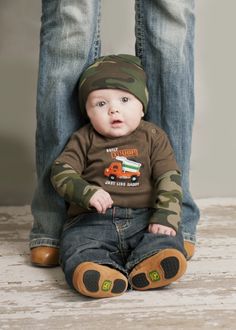 a baby sitting on the ground with his parents legs behind him and feet behind him