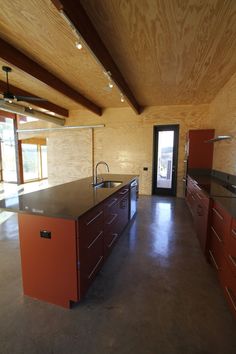 an empty kitchen with red cabinets and black counter tops in a large room that has wood paneling on the walls