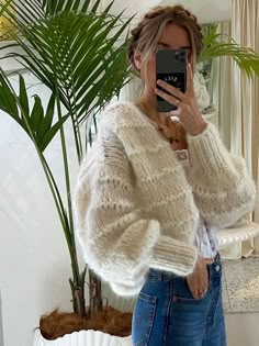 a woman taking a selfie in front of a mirror wearing jeans and a sweater