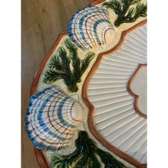 an ornately decorated platter with pine branches and leaves on the rim, sitting on a wooden table