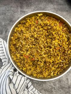 a bowl filled with rice and vegetables on top of a gray tablecloth next to a towel