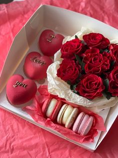 a box filled with macaroons and roses on top of a pink table cloth