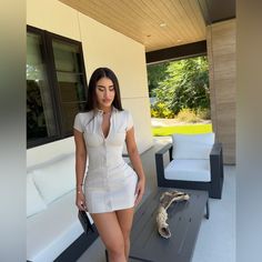 a woman in white dress standing next to a couch and table on the outside patio