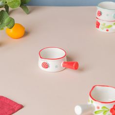 three small cups sitting on top of a table next to an orange and green plant