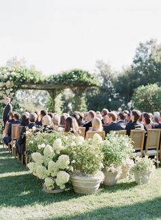 an outdoor ceremony with white flowers and greenery in large urns on the grass