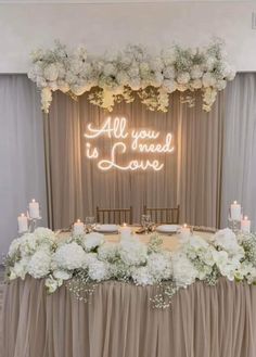 an all you need is love sign on the wall above a table with flowers and candles