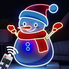 a snowman with a red hat and blue scarf is next to a remote control