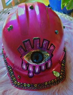 a pink helmet with an eye painted on the side and beads around the rims