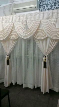 two white curtains with tassels hanging from them in front of a wall mounted air conditioner