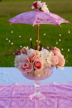 a vase with flowers and an umbrella on a pink table cloth in front of a grassy area