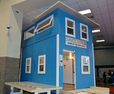 a small blue building with windows on the front and side, sitting in a room under construction