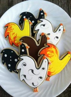 four decorated cookies on a white plate with black and yellow frosting, one in the shape of chickens