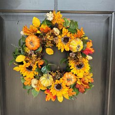 a wreath with sunflowers, pumpkins and leaves is hanging on a door