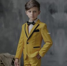 a young boy in a yellow suit and bow tie standing with his hands on his hips