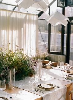 the table is set with plates, glasses and flowers in vases on top of it