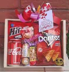 a wooden box filled with candy and snacks on top of a brick wall next to a plant