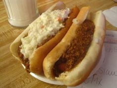 two chili dogs with sour cream on them and a glass of milk in the background