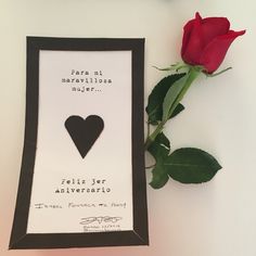 a red rose sitting next to a black and white frame with a heart on it